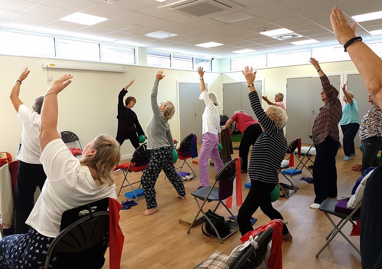 Wide view of the same class standing, everyone reaching one arm up and to the side